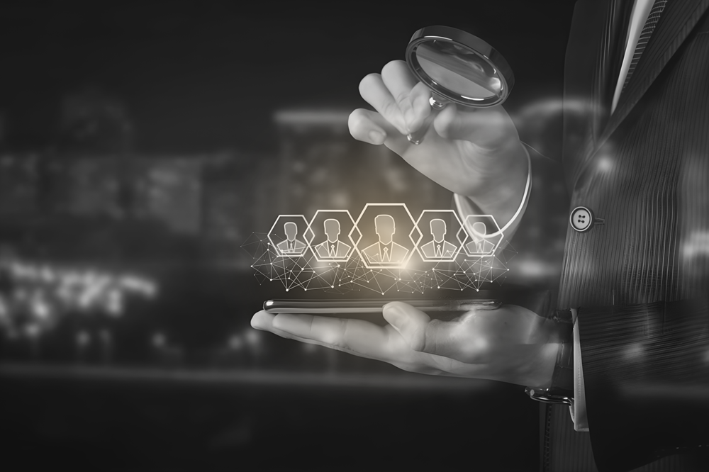 Businessperson in a suit uses a tablet to display a holographic network of user profile icons and a magnifying glass symbolizing search or recruitment.